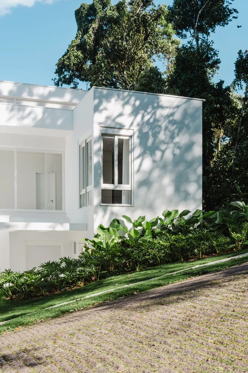 White rendered facade volumes framed by dense tropical foliage and dappled tree shadows