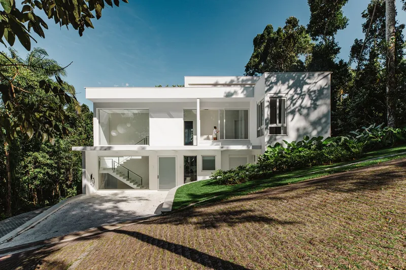 Two-story white rendered facade set into a sloping garden with palm trees and afternoon shadows