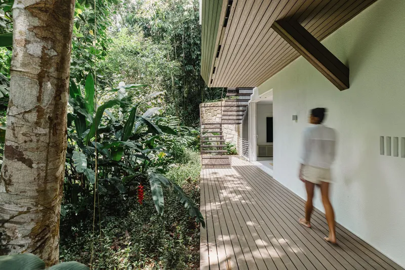 Timber-decked walkway with slatted ceiling overhang leading past planted garden beds with a person in motion