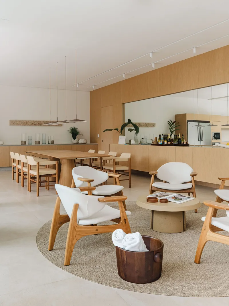 Combined kitchen and dining space with timber cabinetry and mirrored backsplash under linear pendant fixtures