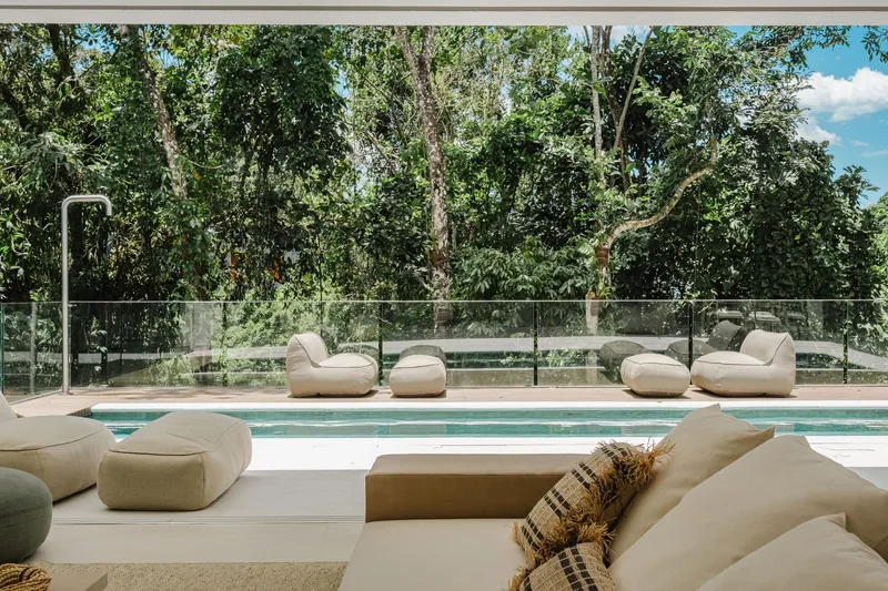 Poolside terrace with glass balustrade overlooking forested hillside on a sunny day