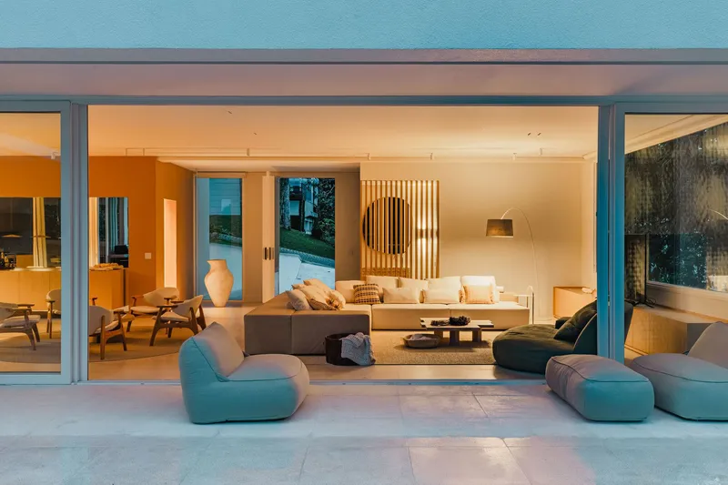 Open living room at dusk with full-height glazing connecting interior seating to the terrace