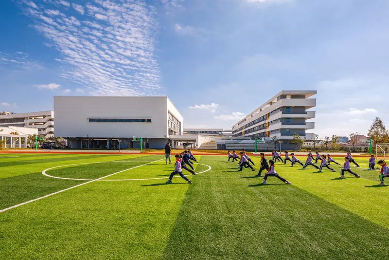 Students exercising on the football pitch with the white volume and residential blocks beyond