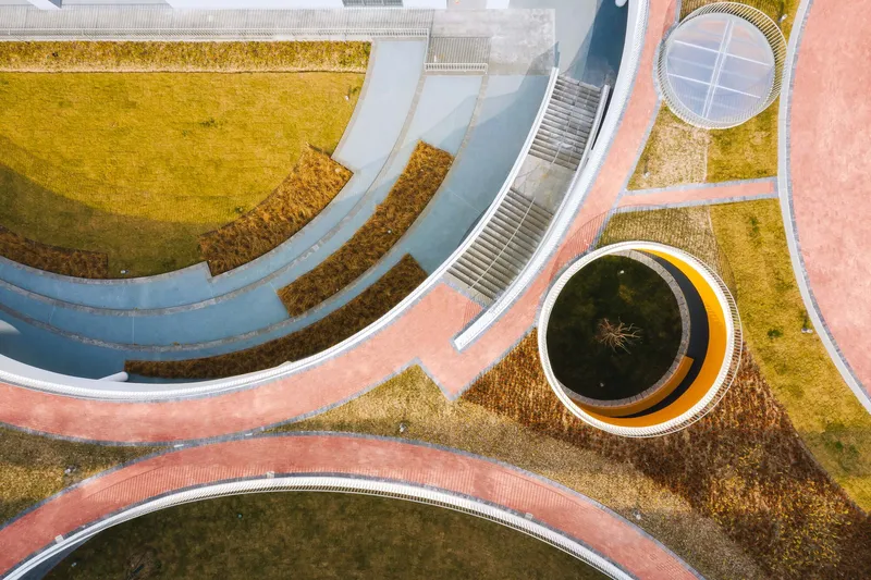 Aerial view of curved pathways, circular skylights, and planted areas with pink and grey paving