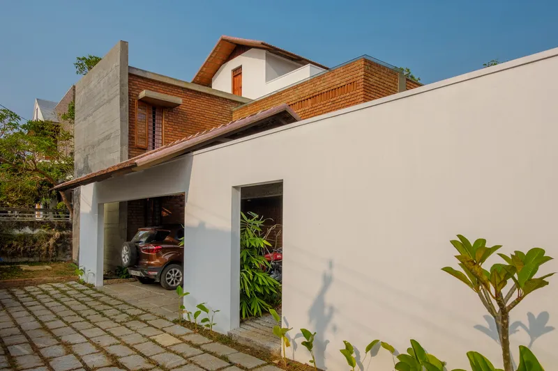 White plastered garage wall with gridded paving and young plantings along the entrance path