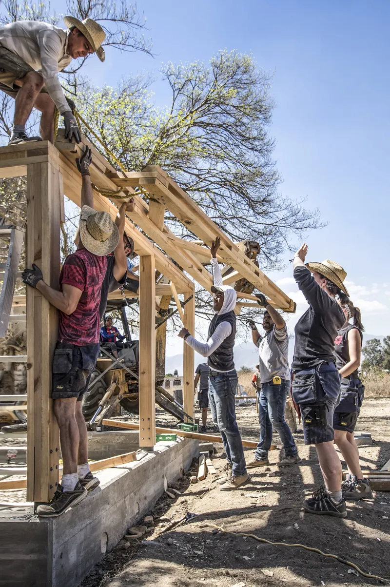Group of builders lifting a timber roof beam into place on a concrete foundation