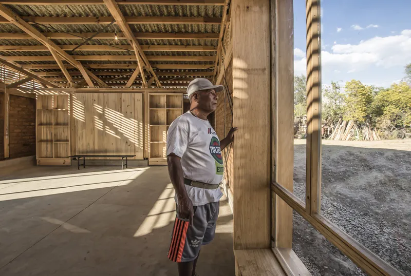 Covered timber pavilion with a person standing near slat wall openings on a sunny afternoon