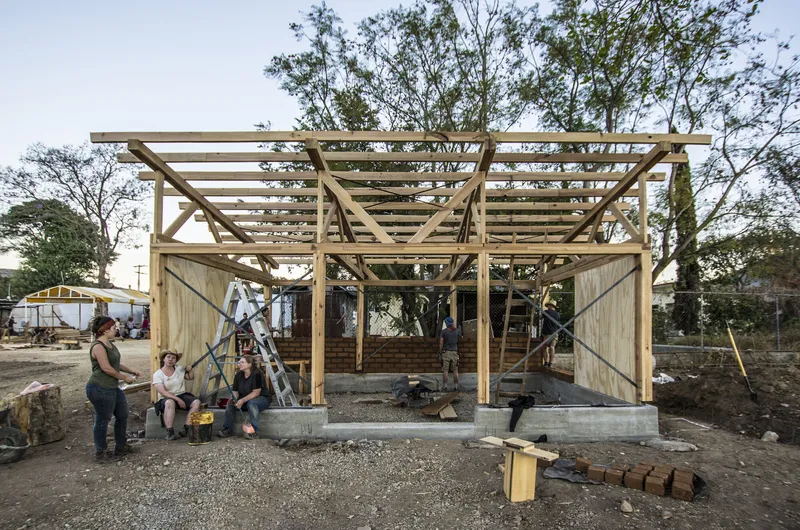 Construction workers resting beneath the exposed timber roof frame with diagonal bracing during late afternoon