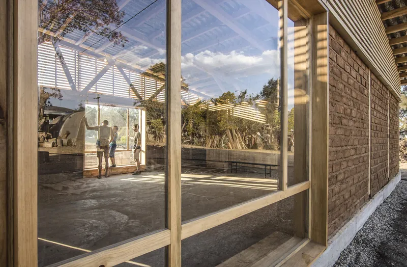 Glass-walled corridor with timber frame and slatted roof overhang casting striped shadows on concrete floor