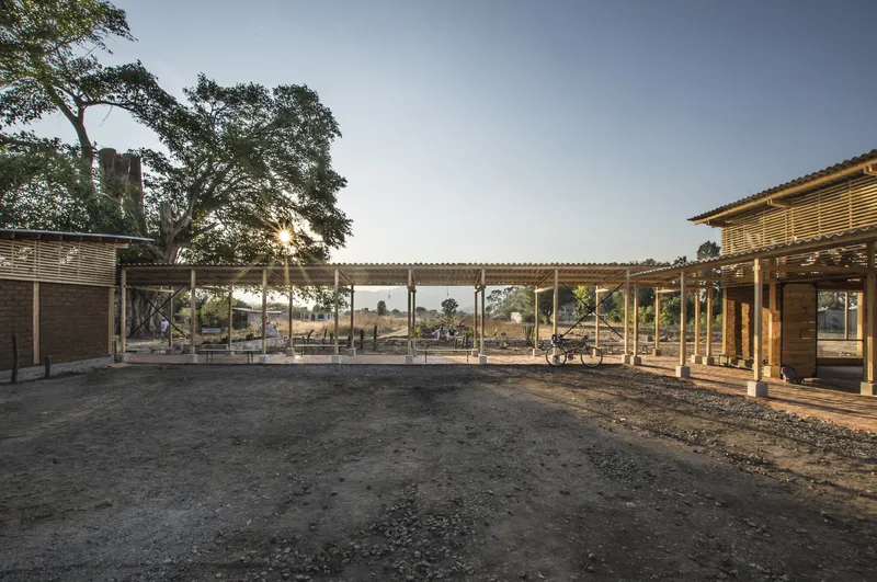 Covered courtyard space with corrugated metal roof and timber columns viewed at dusk with surrounding landscape