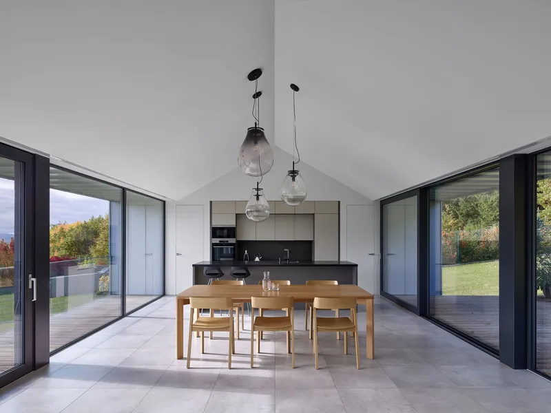 Open dining area with timber table and glass doors to exterior terraces beneath a vaulted white ceiling