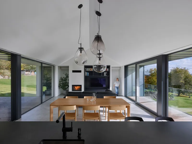 Interior view through dining and living spaces with glass pendant lights and a person visible on the exterior deck