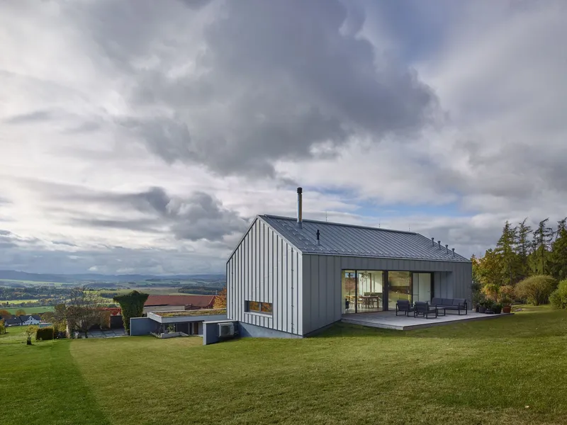 Vertical metal-clad gable volume rising from a sloped lawn under heavy autumn clouds
