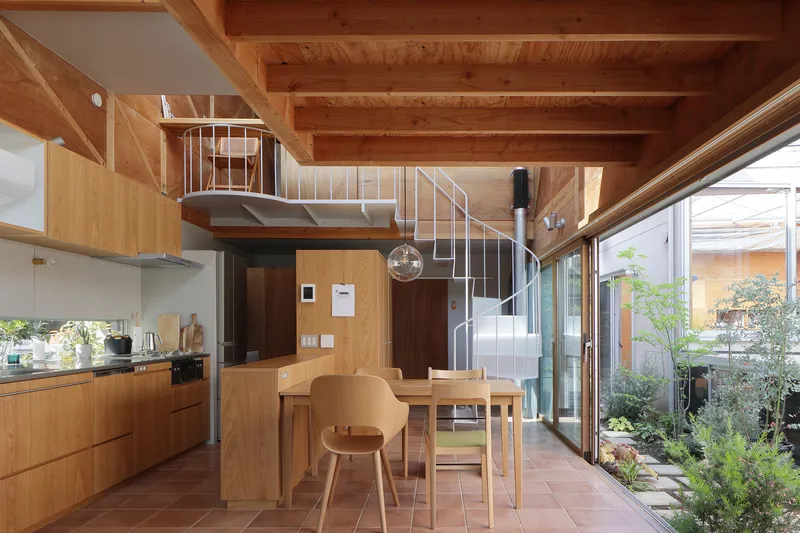 Open-plan dining area with timber beams, spiral staircase and glazed doors to a planted courtyard