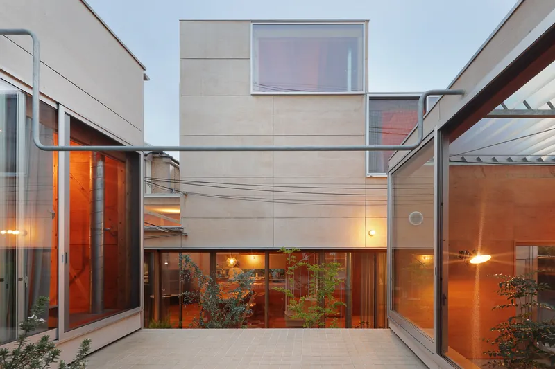 Courtyard view with light-toned plywood panel facades and glass walls glowing at dusk