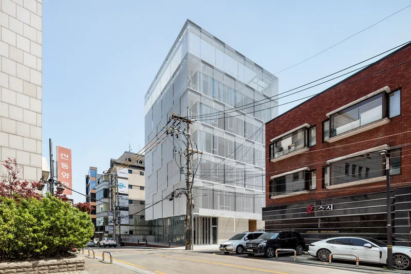 Street view of the translucent facade with parked cars and overhead power lines crossing the frame