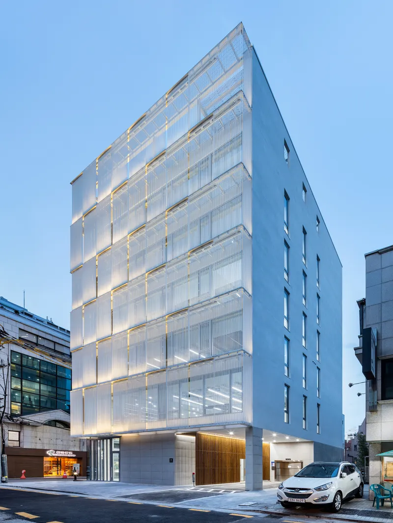 Corner view at dusk showing the illuminated facade with warm interior lighting glowing through translucent panels
