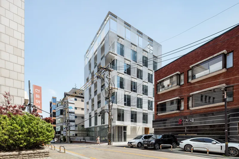 Street view of the white ribbed facade flanked by red brick buildings and utility poles