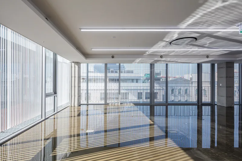 Interior view of an empty floor with vertical louvered facade casting striped shadows across polished stone