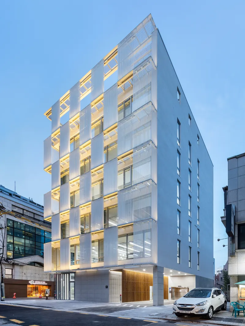 Street view of the white louvered tower facade illuminated at dusk with parked cars in front