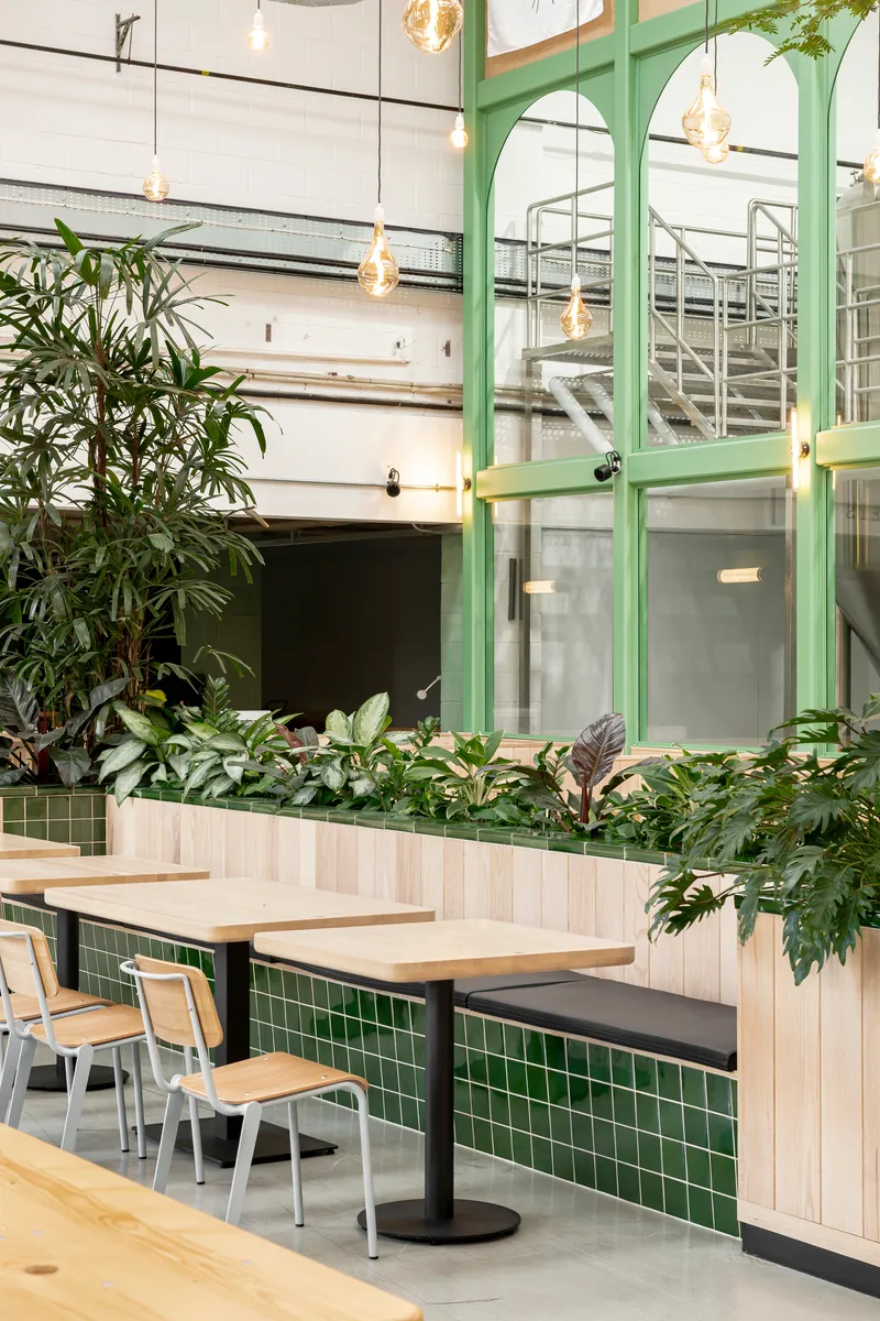 Interior seating area with light wood booths, green tile base and painted green steel partition framing