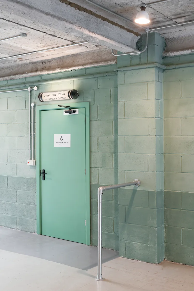 Mint green steel door with exposed conduit and concrete block walls under an industrial ceiling