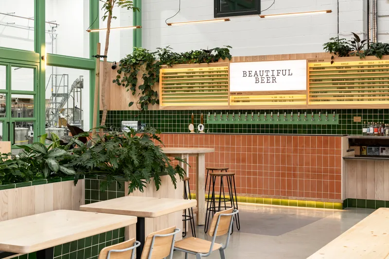 Bar counter clad in terracotta and green tiles with planted beds overhead and illuminated menu boards above