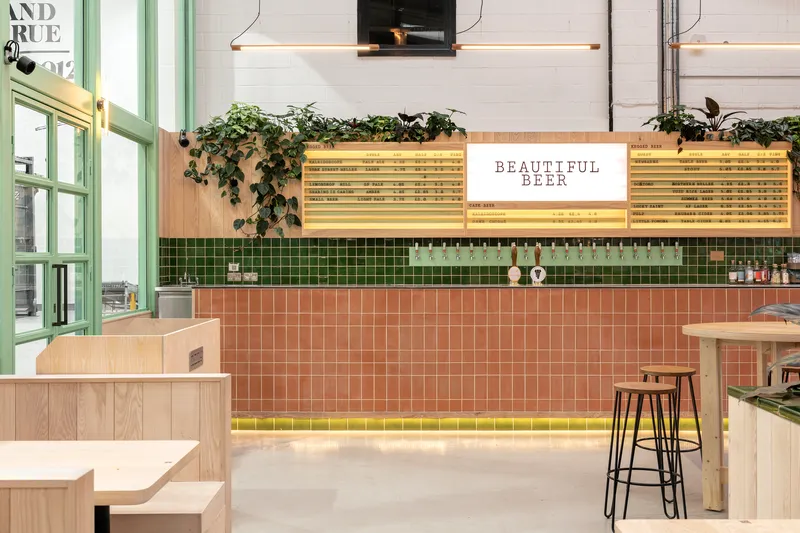 Frontal view of the tiled bar with timber-framed backlit signage and hanging plants cascading from planter boxes