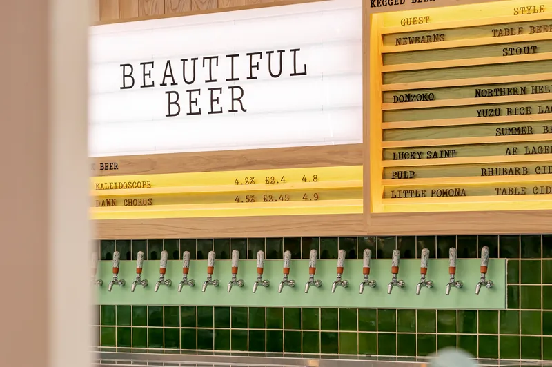 Close-up of the tap wall with chrome beer taps set into green square tiles beneath backlit menu boards