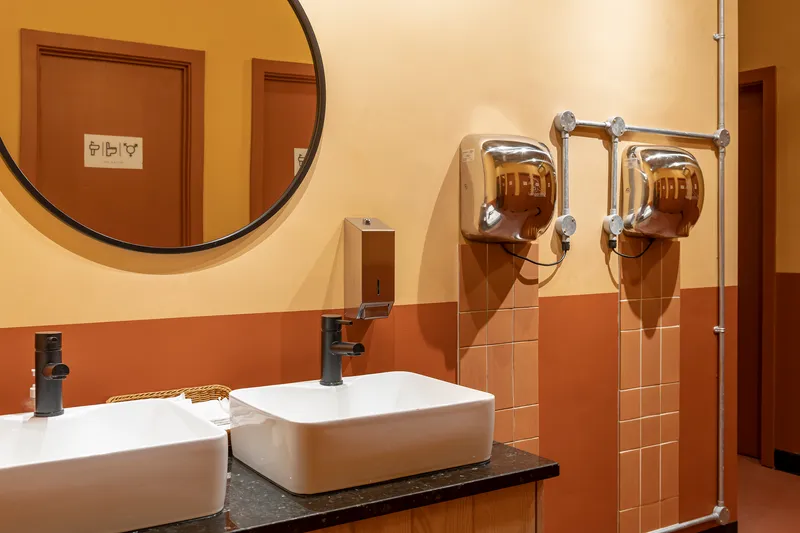 Restroom vanity with twin white basins and chrome hand dryers against terracotta tiled walls