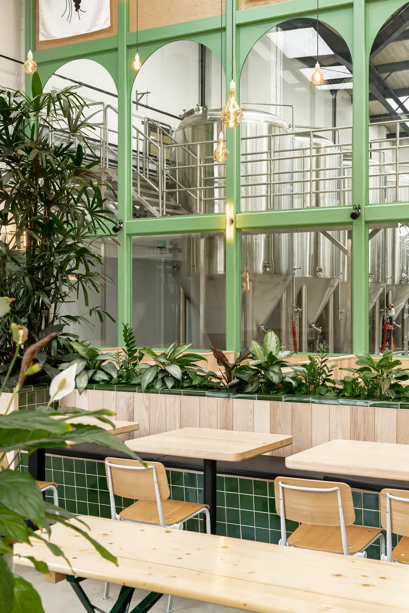 Seating area with timber benches and green tile plinth facing brewery tanks behind glazed screens