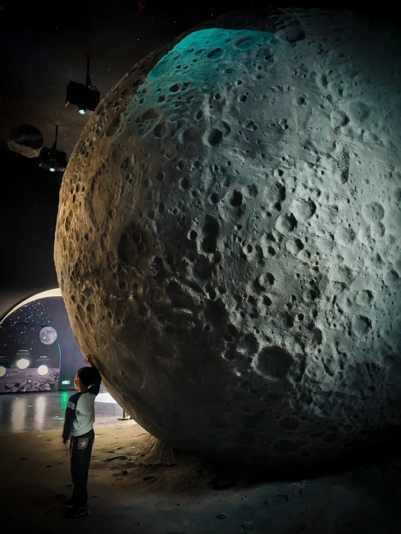 Interior gallery space with a visitor viewing an illuminated spherical lunar surface installation