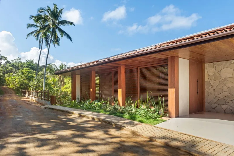 Long facade with timber columns and louvered screens along a planted bed with palm tree overhead