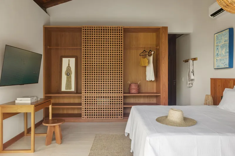Bedroom with latticed timber storage wall and white bed under exposed wood ceiling beams