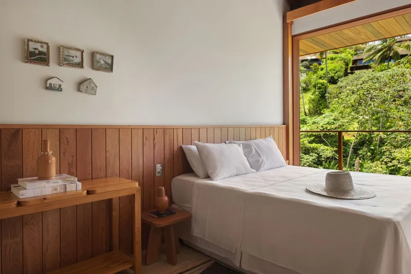 Bedroom with vertical timber paneling and large opening framing vegetation outside