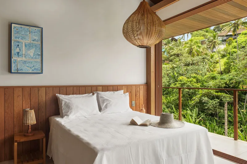 Timber-lined bedroom opening with woven pendant light and balcony overlooking tropical foliage