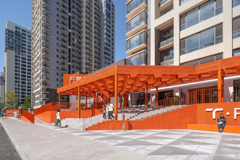 Orange steel canopy with coffered underside sheltering plaza steps at base of residential tower under clear sky