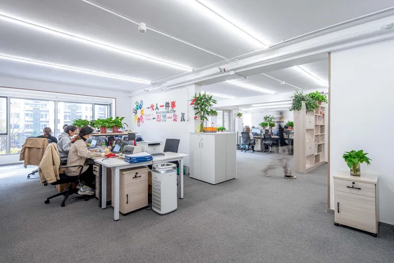 Open plan office with exposed ceiling beams and potted plants between workstations