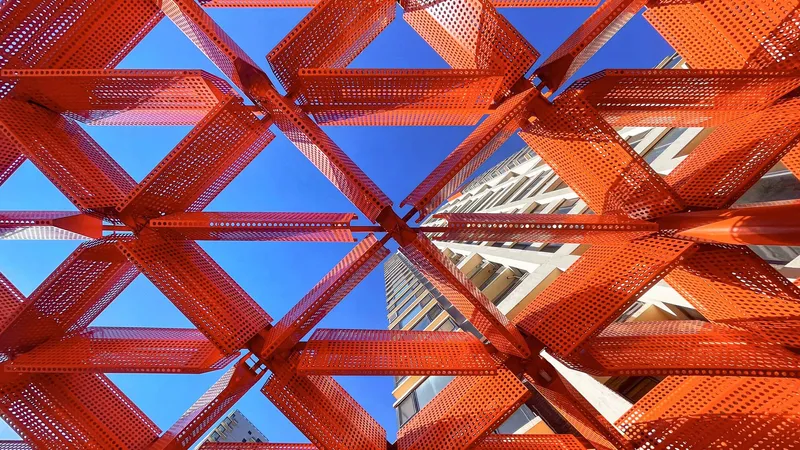 Looking up through the perforated orange steel lattice framework against a clear blue sky