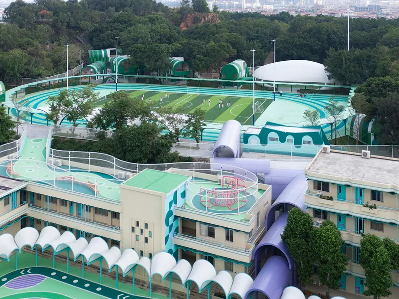 Aerial view of the terraced campus with curved running track and domed canopies among tree canopies