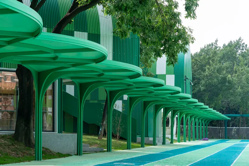 Repeating green arched canopies with ribbed undersides extending along the planted edge of the playground