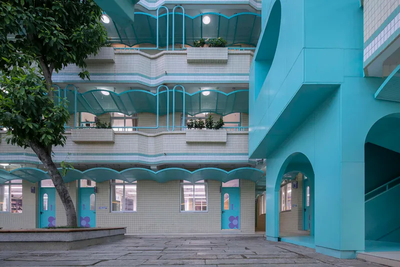 View across a paved plaza showing tiered balconies with wavy white railings and potted trees