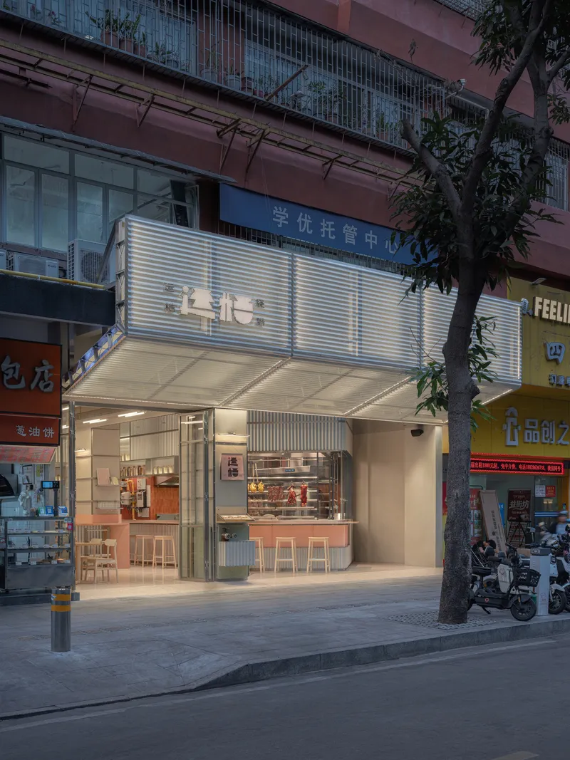 Angled view of the shopfront facade showing corrugated metal panels and glazed opening at twilight