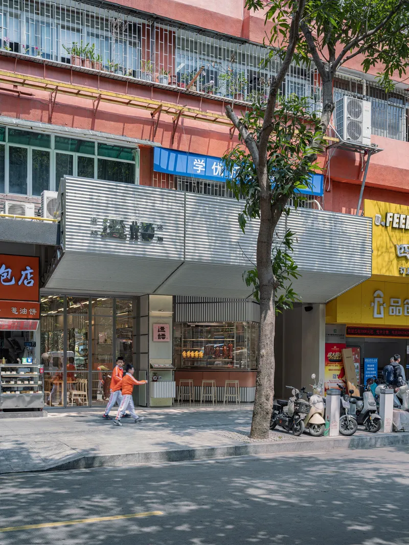 Street view of the restaurant facade with corrugated metal canopy and tree casting shadows on the pavement