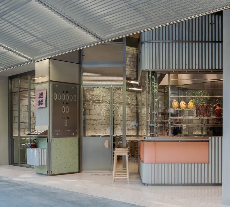 Entrance detail showing pale green folding door, exposed brick wall and corrugated metal cladding in daylight