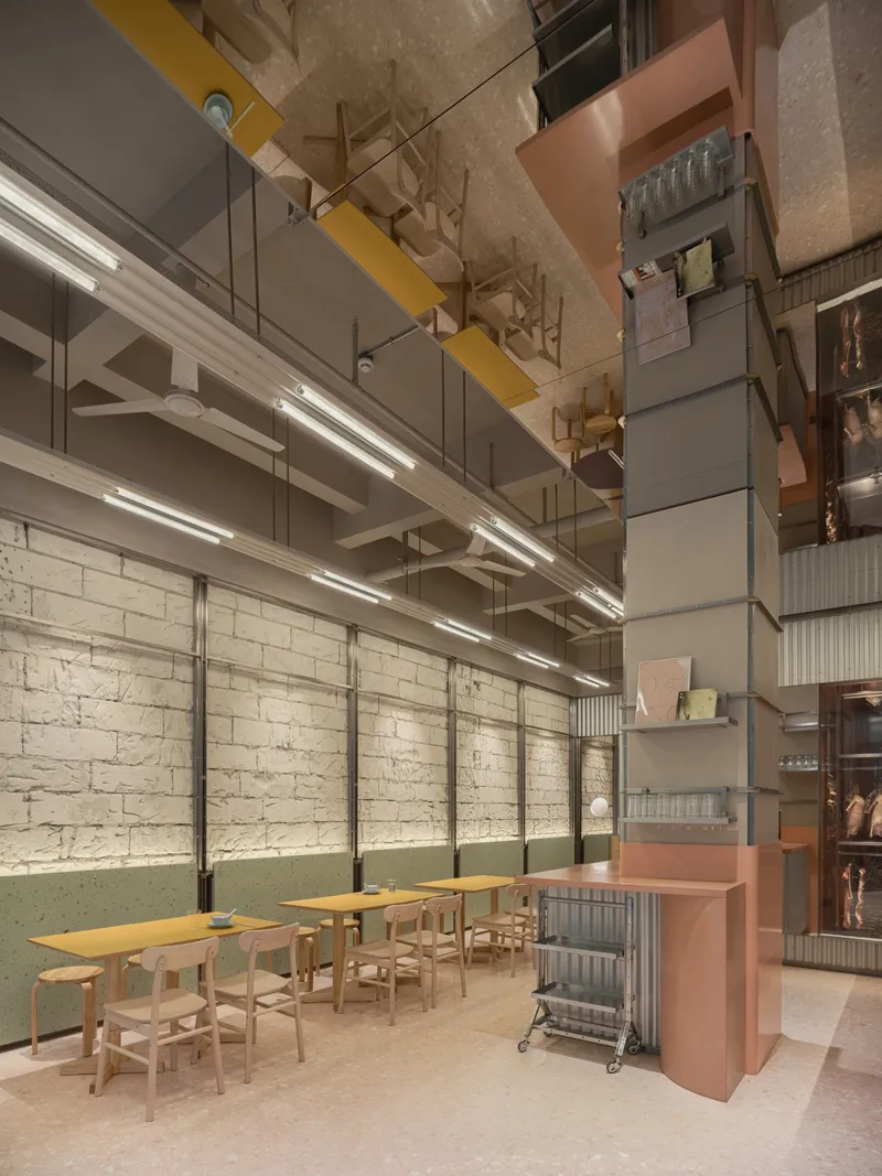 Dining area with blonde wood tables, suspended linear lighting and illuminated brick wall under reflective ceiling