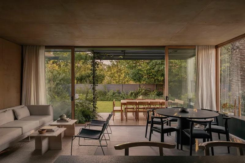 Living area with board-formed concrete ceiling opening to covered terrace and lawn beyond