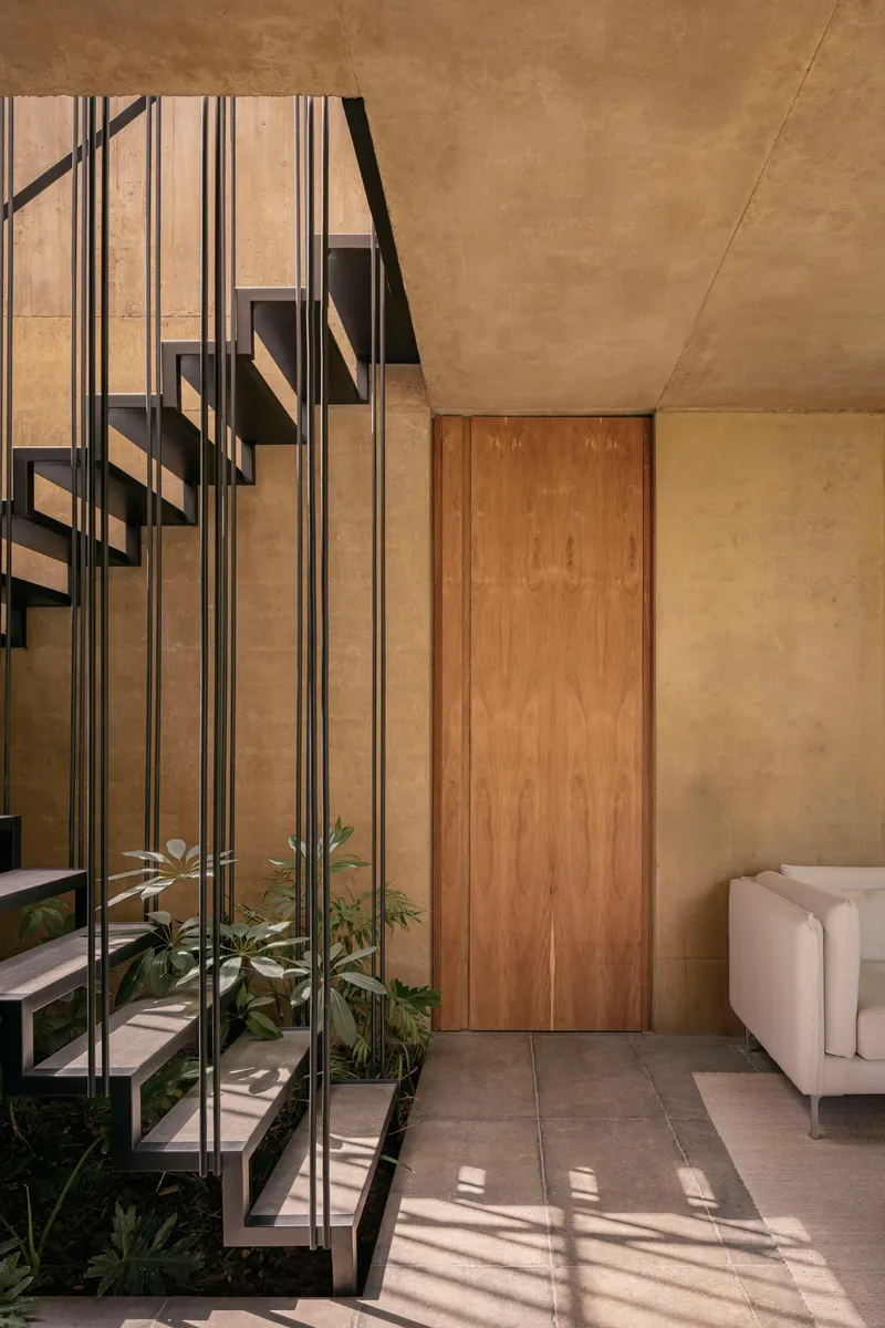 Steel staircase with potted plants beneath casting dappled shadows on the tile floor