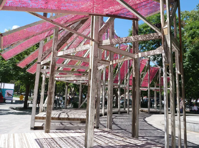 Interior view beneath the angled timber frame structure showing cross bracing and translucent pink canopy overhead