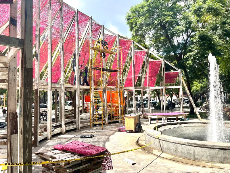 Construction scaffolding beside the pavilion structure with circular fountain and spray visible in afternoon light